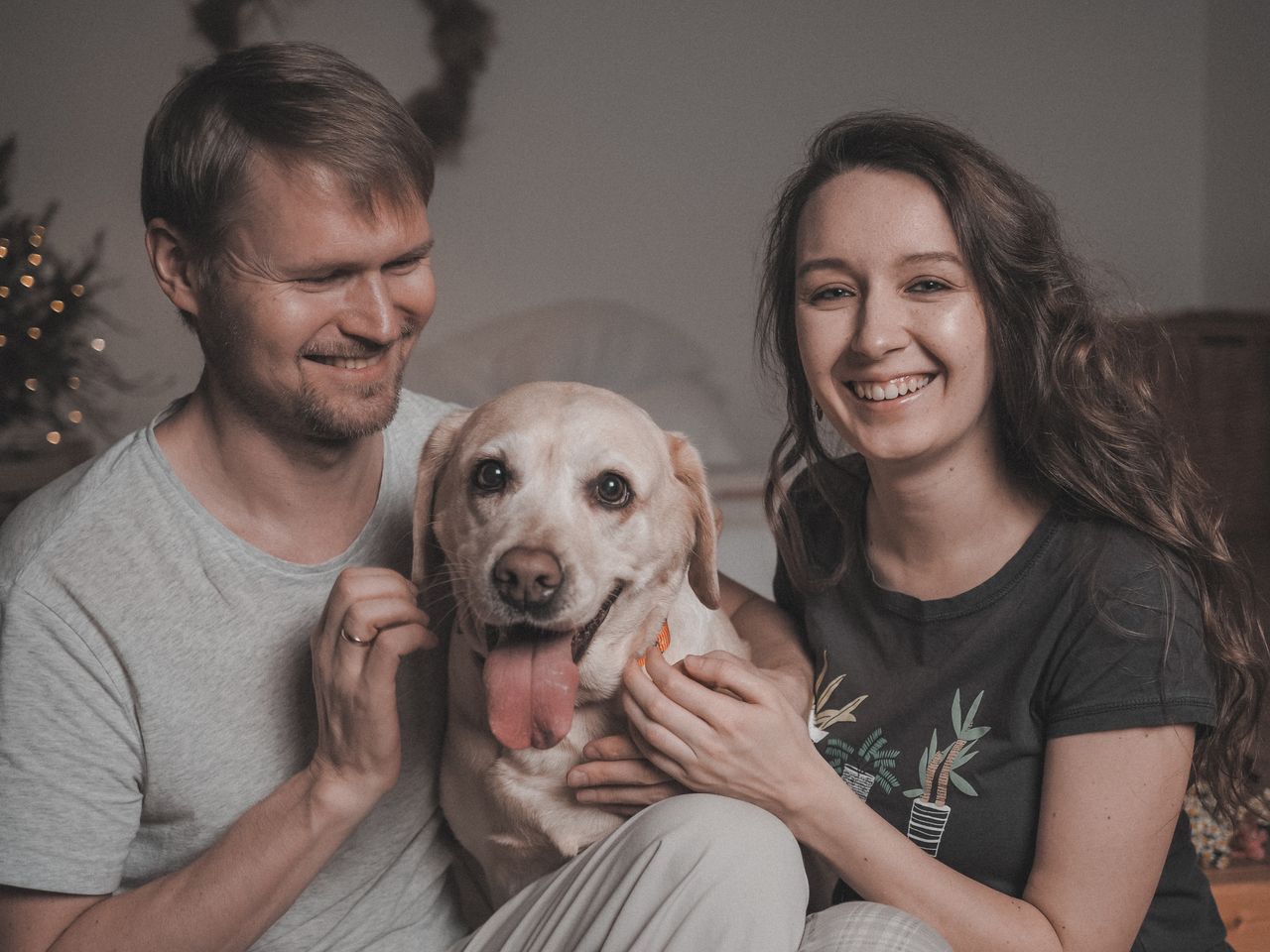 Happy couple playing with their Labrador dog at home, showcasing love and companionship.